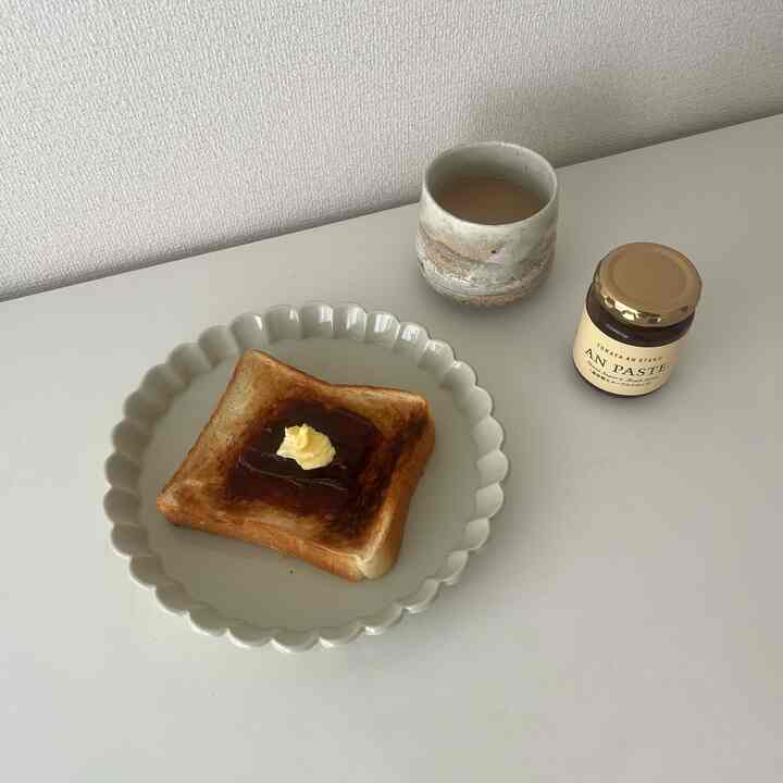 白いトーンのキッチンテーブルに、バターとあんこがのったトーストが乗ったシンプルな皿とお茶のある朝食のある雰囲気のあるインテリア