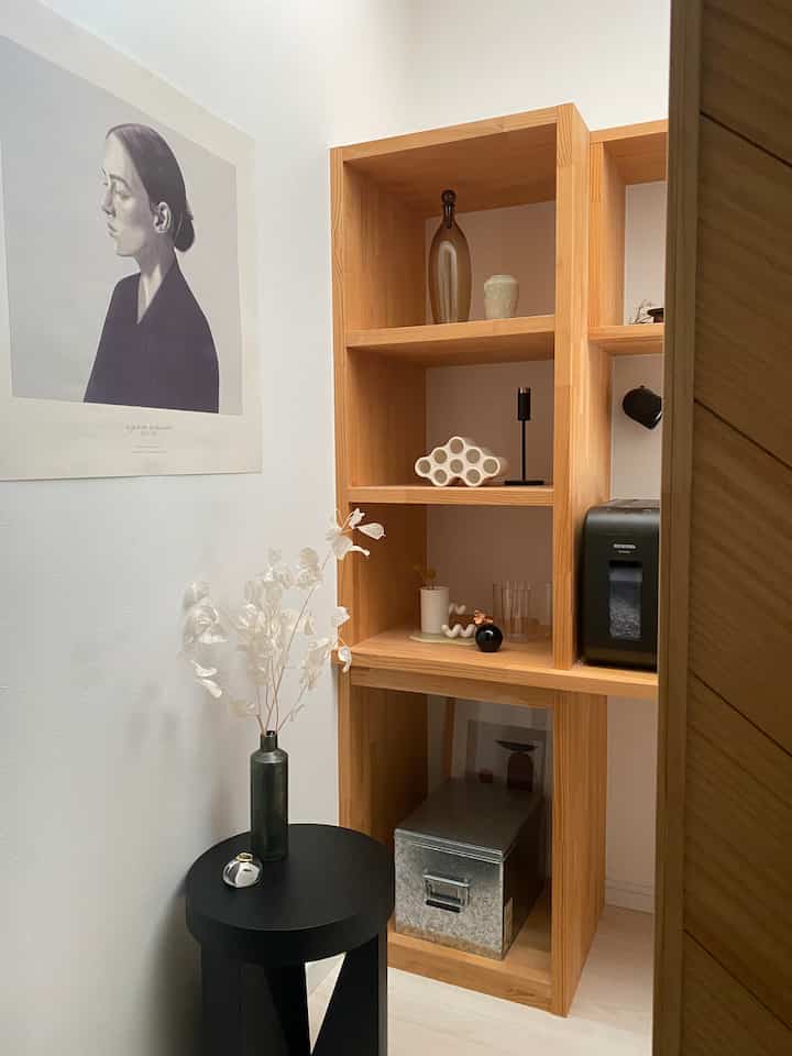 ナチュラルな木目調の棚と白い壁、黒いサイドテーブルが配置された落ち着いた印象の玄関スペース