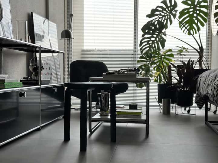 Modern living room in black and gray tones featuring a black stool and table center, with black USM HALLER storage on left, creating a sleek atmosphere