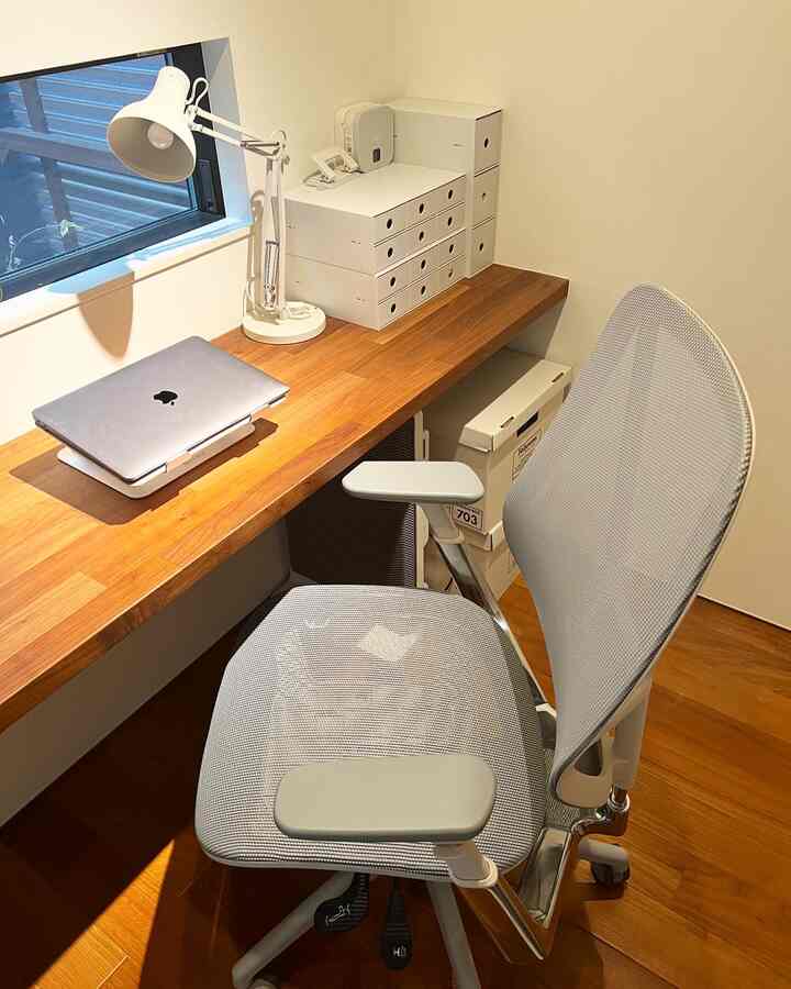 ライトブラウンの木製デスクと白い壁のシンプルで清潔感のあるホームオフィス空間、グレーのオフィスチェアが配置されている