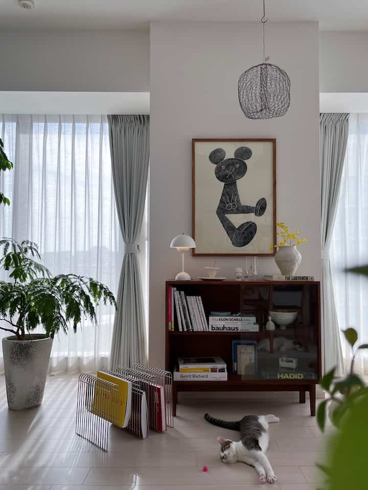 明るいナチュラルカラーのリビング、中央右側にヴィンテージ風の本棚が配置され、床には2匹の猫が横たわっている印象的な空間