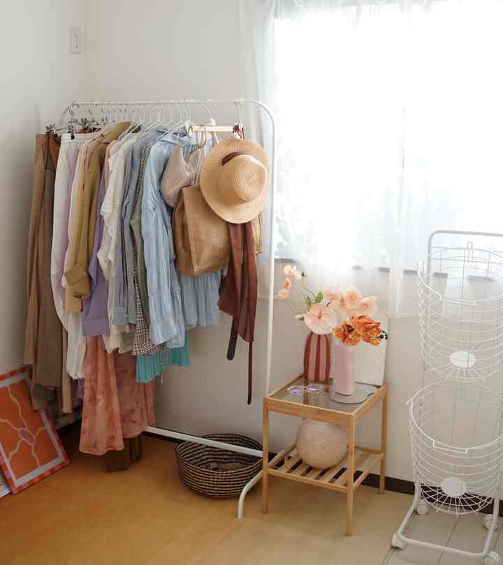 Small dressing room with white walls, orange floor, light brown side table and clothing rack organized neatly