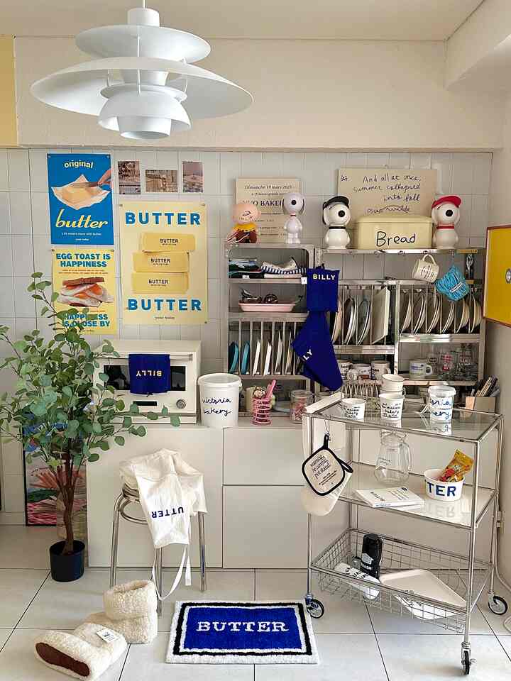 Kitchen space with white tiled walls and floors, blue accents, a pendant light, metal trolley, and a butter-themed rug creating a cozy atmosphere