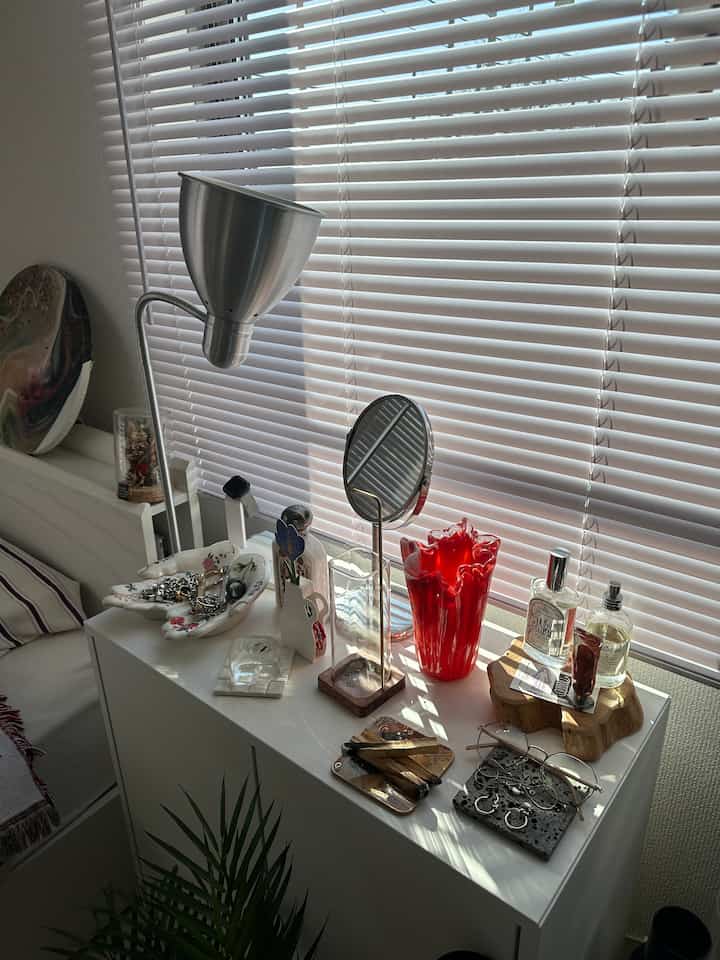 白を基調としたリビングルームの空間、収納キャビネットの上に様々なオブジェが配置され、シルバーのフロアランプと白いブラインドが印象的なインテリア