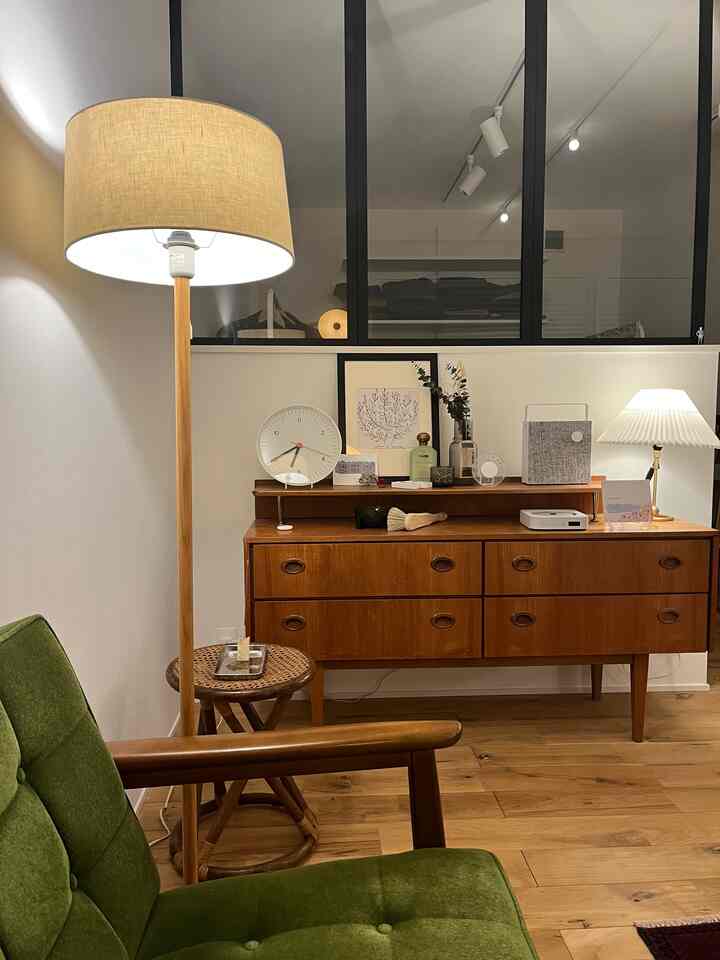 ナチュラルな色調のリビング、木製キャビネットとラタンのスツール、グリーンのソファが落ち着いた雰囲気を演出する空間