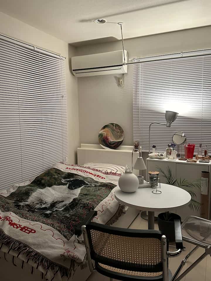 白を基調としたコンパクトな寝室、シングルベッドとラタンチェア、間接照明が印象的な空間