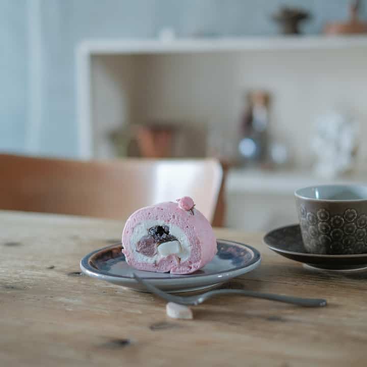 A warm home cafe dining room with soft beige and wood tones featuring a pink cake roll and a teacup on wooden table