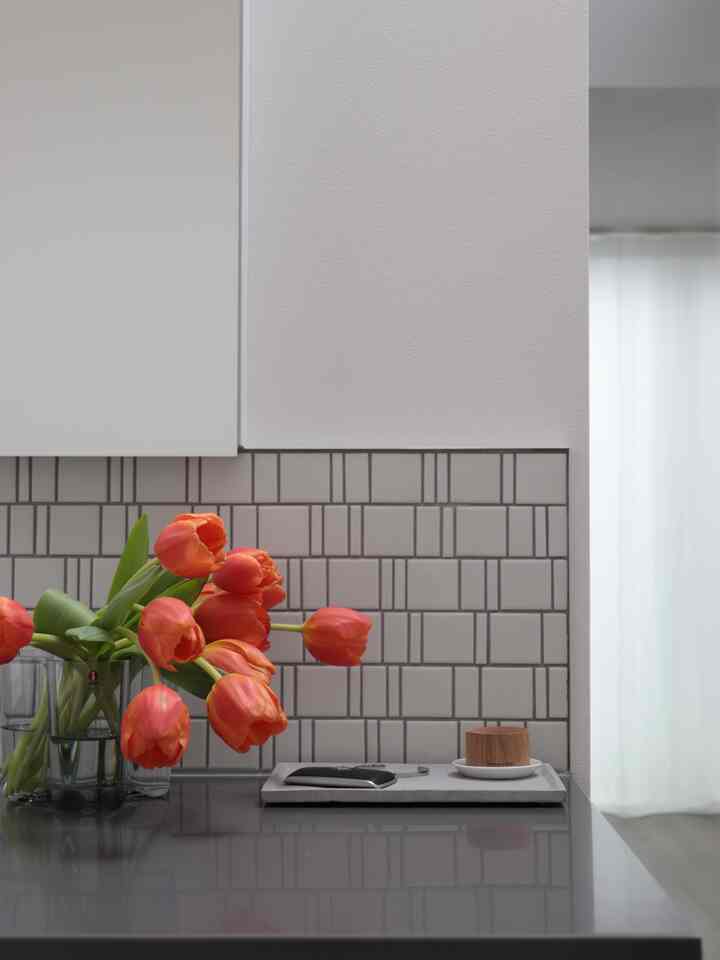 白とグレーのトーンのキッチン、中央に鮮やかな赤いチューリップの花束とアロマウッドが置かれた、シンプルでモダンな雰囲気のあるインテリア