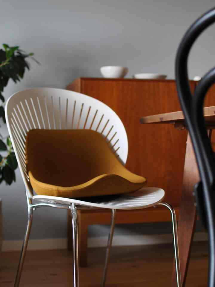 白いフレームに茶色いクッションのアームチェアがナチュラルトーンのキッチン空間のダイニングテーブル脇に配置されている