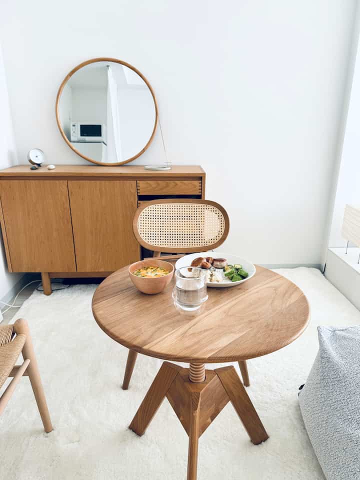 白い壁とラグが印象的なワンルーム、木目調のダイニングテーブルとラウンジチェアが配置された自然で落ち着いたインテリア