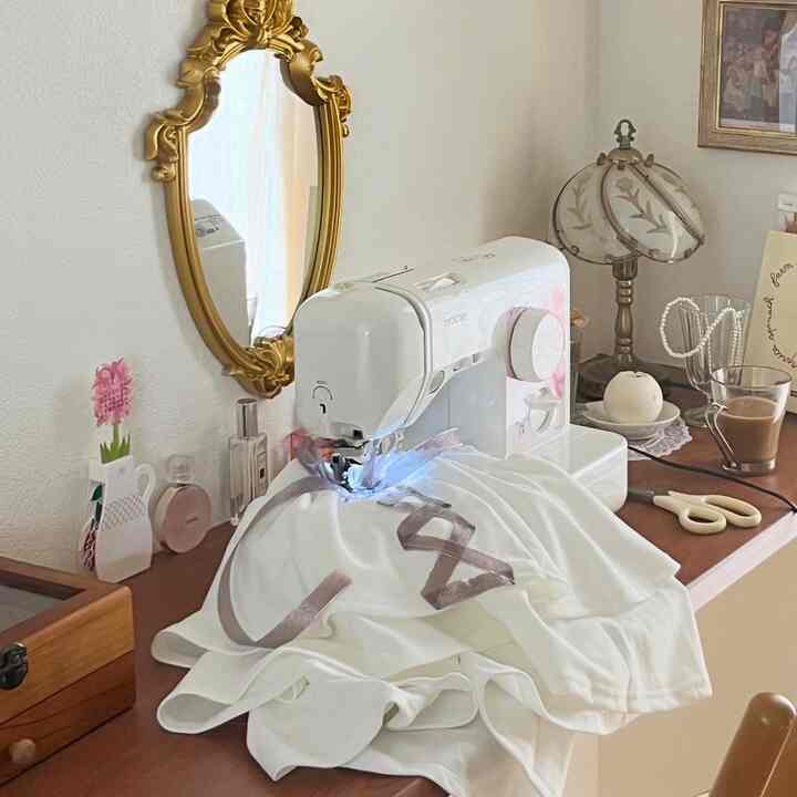 ホワイトとウッドトーンのフレンチカントリースタイルの小さなデスク、中央にミシンとヴィンテージ風ミラーが配置されたミニマルな作業スペース