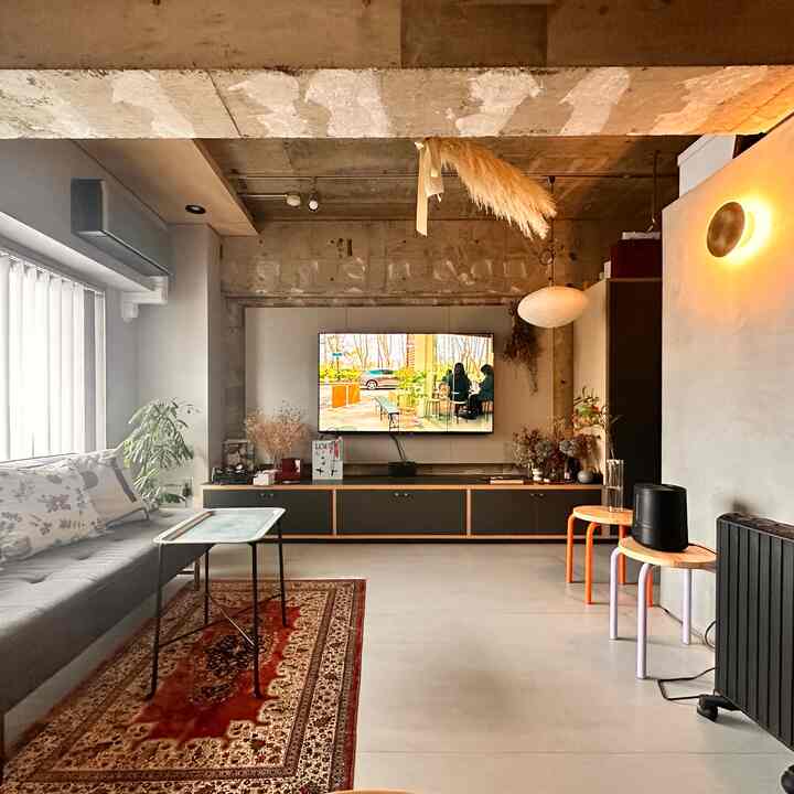 モダンなコンクリート天井とグレーのソファ、テレビ台が配置された温かみのあるリビング空間