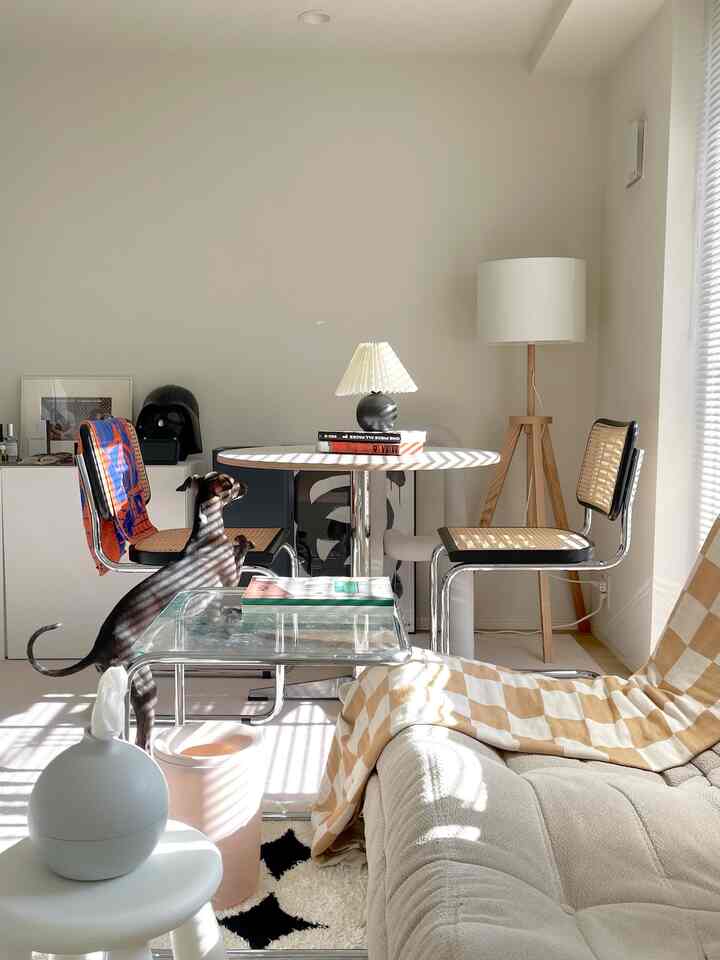 Bright white-walled living room featuring beige sofa, natural woven chairs, and wooden floor lamp creating a cozy atmosphere