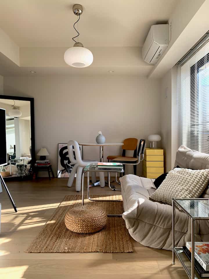 ホワイトとウッドトーンの調和が取れたミニマルなリビング兼ダイニング、クリーム色のソファと丸いダイニングテーブル、大きな全身鏡が配置された印象的な空間