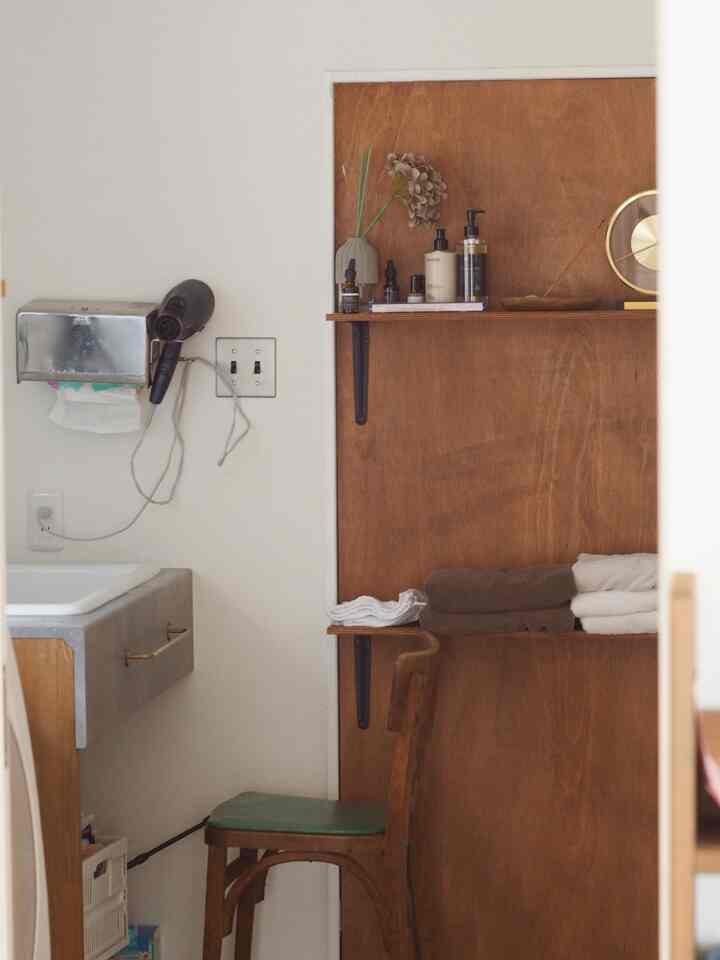 ブラウンの木目調の壁とホワイトが調和したお手洗い、木製の椅子とタオル、化粧品が配置された雰囲気のあるインテリア