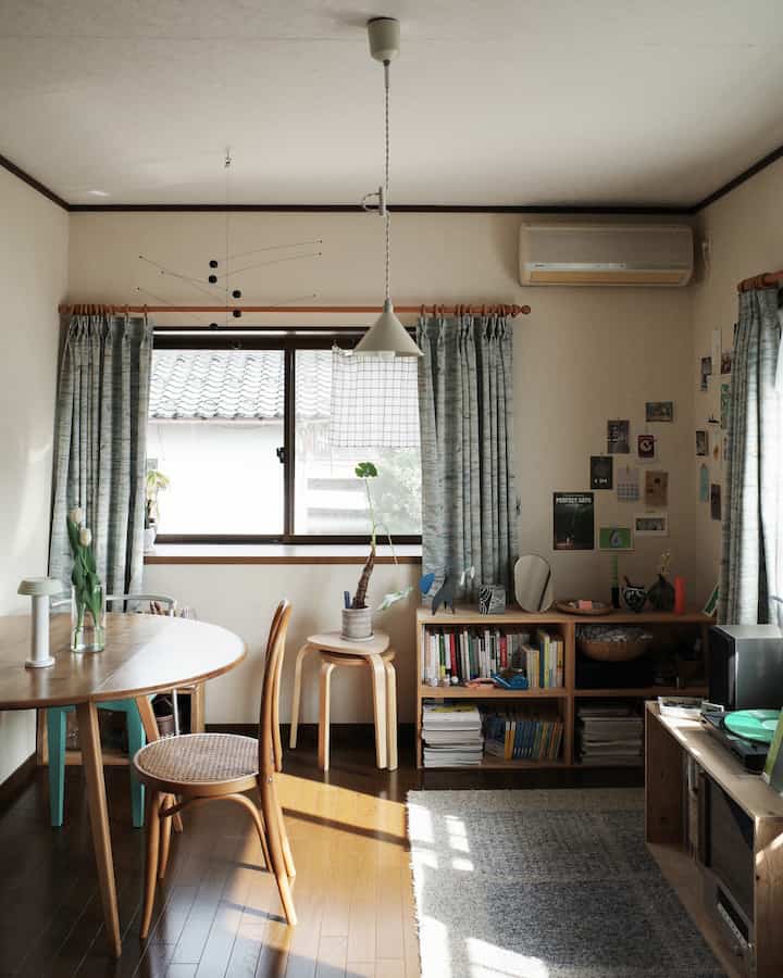 Natural wood tones and soft blue curtains in a Nordic living room featuring bookshelves and dining area with cozy ambiance