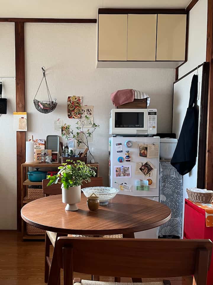 ベージュの吊り戸棚と木製家具が配置された一人暮らし用のコンパクトなキッチン、テーブル上の植物が雰囲気を演出する空間
