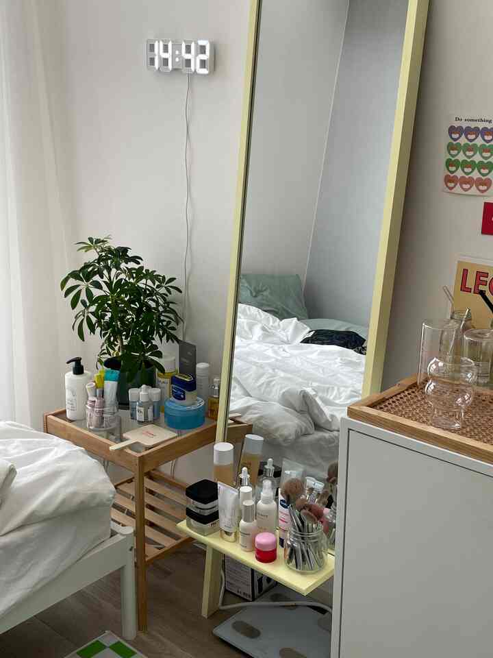 White and natural color toned bedroom space featuring a large full-length mirror and various skincare products in a tidy setting