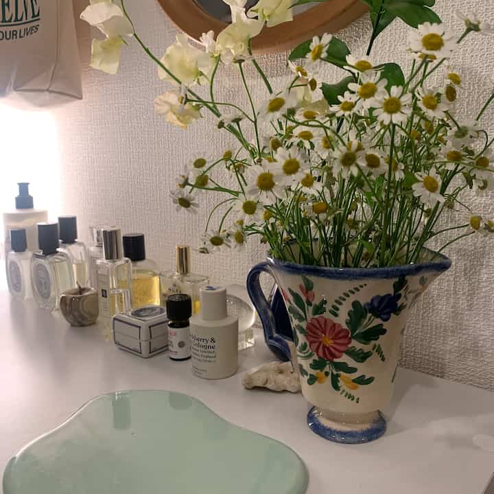 白を基調とした空間、化粧台の上に香水瓶と花瓶があり、自然な雰囲気のあるインテリア