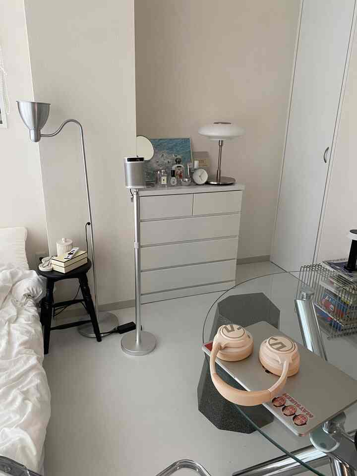 白とシルバーのトーンでまとめられたコンパクトな寝室、ベッドやナイトテーブル、フロアランプが配置されたモダンで清潔感のあるインテリア