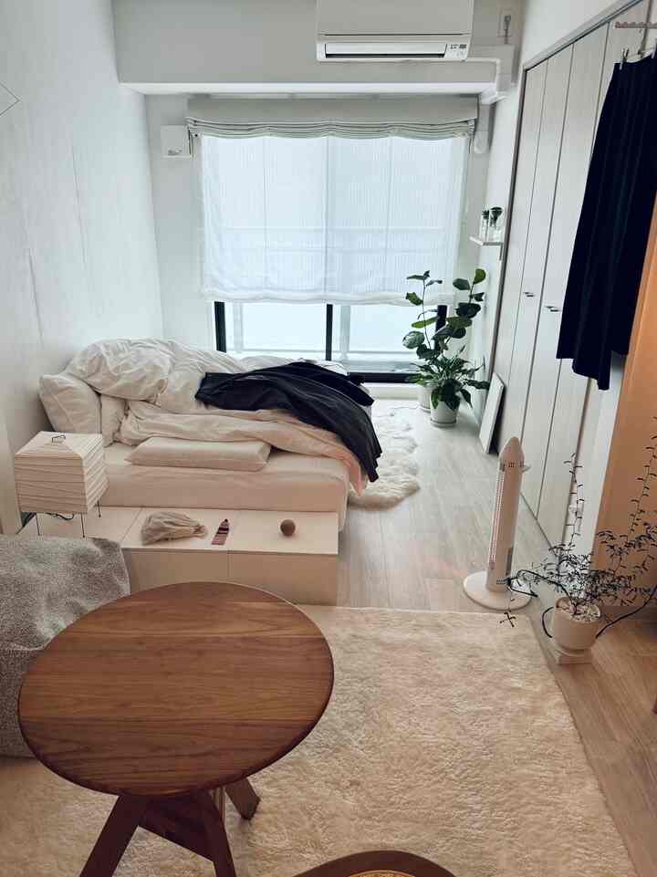 ホワイトとウッドトーンの調和があるワンルームのリビング、ソファベッドとカーテンが配置されたミニマルなインテリア