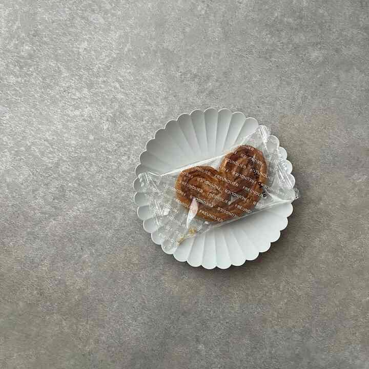 A white scalloped plate with packaged bread rests on a gray concrete textured surface, showcasing natural tones.