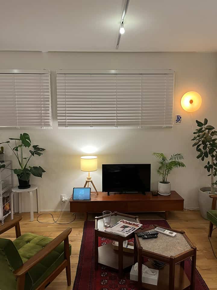 ナチュラルトーンのリビング、木目調家具と赤いヴィンテージラグ、緑のアームチェアと植物が配置された落ち着いた雰囲気のインテリア