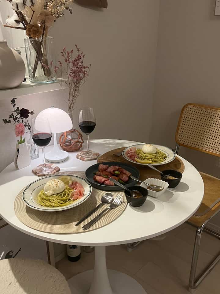White-toned compact dining table and chairs with a white table lamp and wine glasses, showcasing a natural and simple two-person dining space