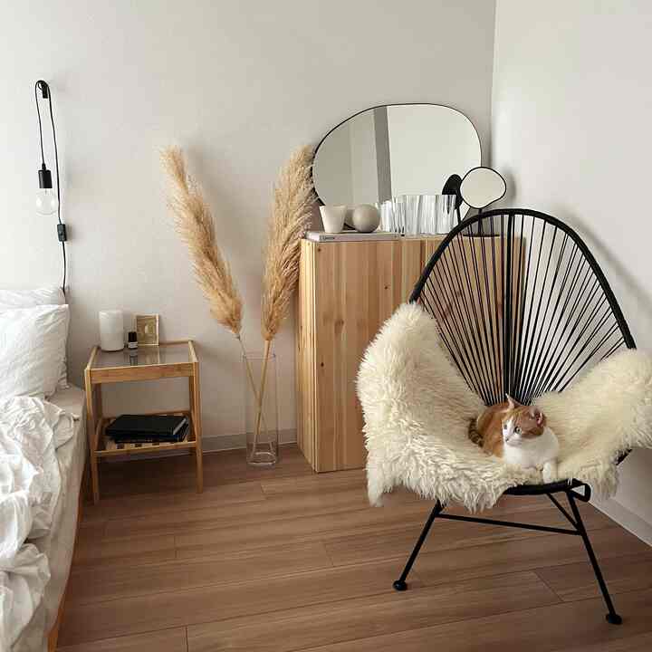 ベージュと木目調の落ち着いた一人暮らしの寝室、黒いアームチェアに猫が座り、自然素材のインテリアが配置された空間
