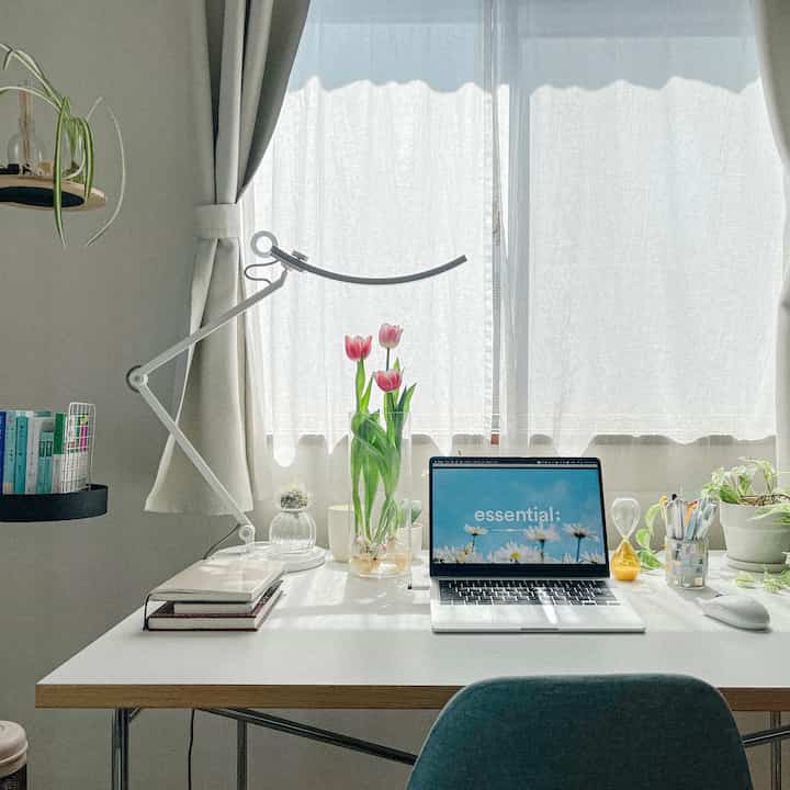 白とナチュラルカラーの明るいホームオフィス、ピンクのチューリップの花瓶とノートパソコンが置かれた印象的な作業空間