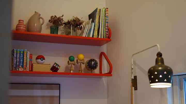鮮やかな赤い壁棚に書籍と装飾品が配置された小さな北欧風のワークスペース