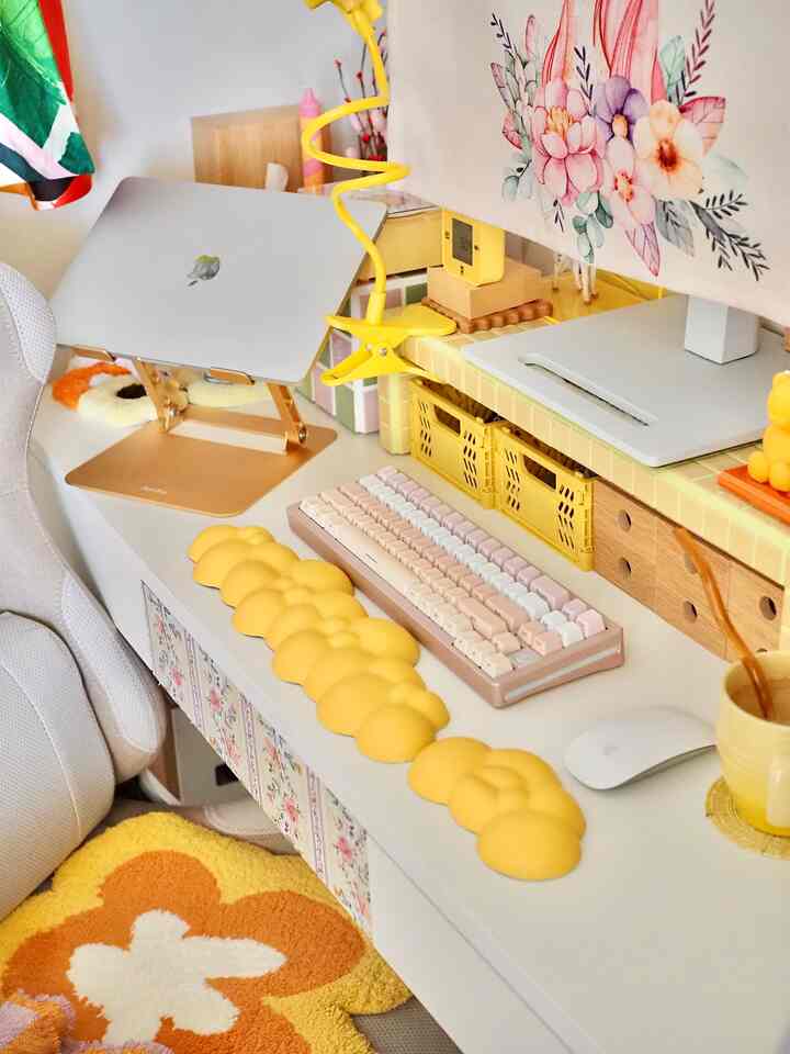 パステル調のホームオフィス、ノートパソコンスタンドやパステルカラーのキーボード、黄色のリストレストが配置された雰囲気のある作業空間