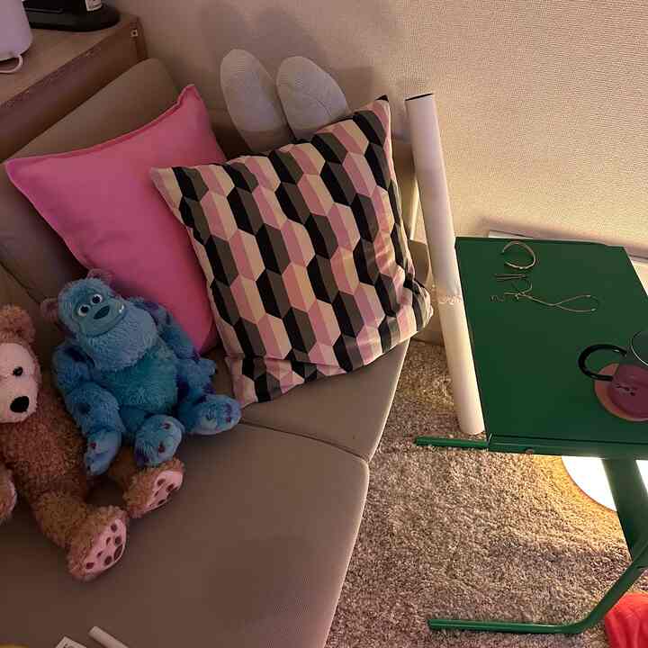 ベージュのソファにピンクと幾何学模様のクッションが置かれた子供部屋風の居心地の良い空間、緑のサイドテーブルとラグが調和している