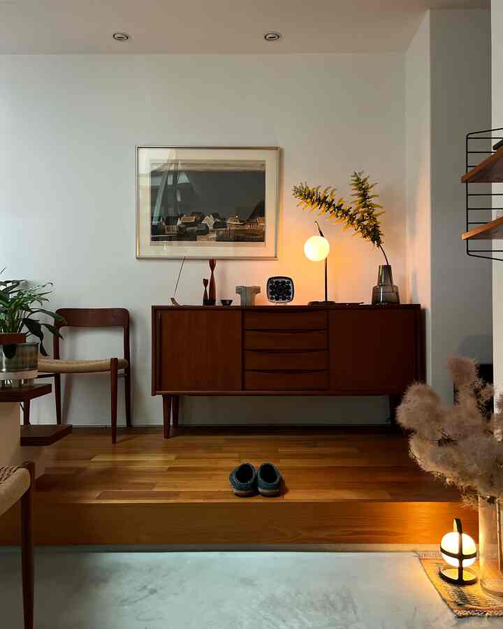 White walls and warm brown wood-toned sideboard with armchair in a cozy, hotel-like Nordic style living room