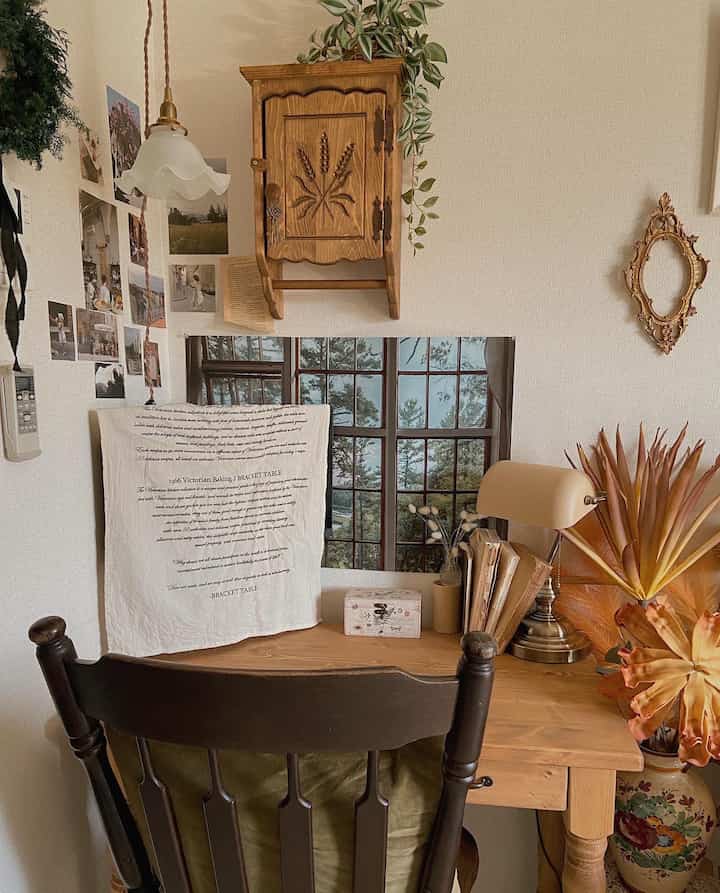 A cozy home office corner in a living room with wood tones and natural decor featuring a wooden desk and vintage table lamp