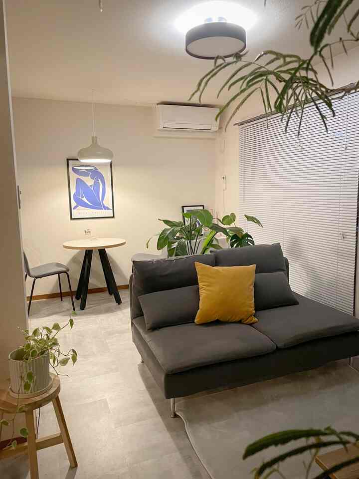 淡いベージュのトーンのリビングとダイニング、ダークグレーのソファにマスタードクッション、ダイニングテーブルと椅子が配置されたモダンな空間