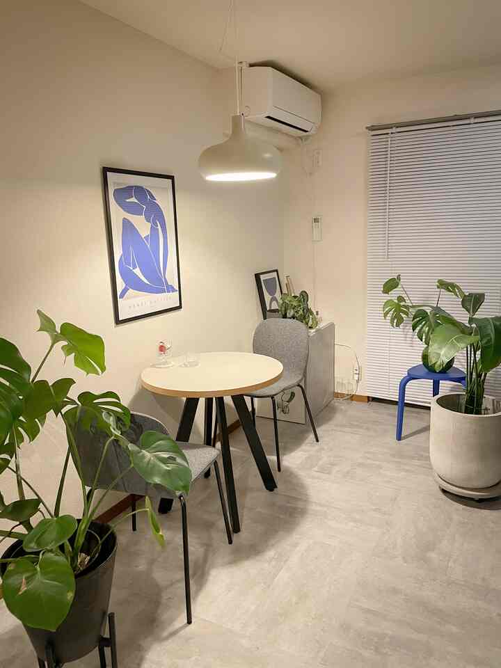 白とグレーのトーンのモダンなリビング、中央に小さな丸テーブルと椅子2脚、複数の植物が配置された清潔感のある空間