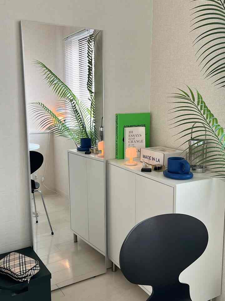 白と緑の色調のリビング、 大きな全身鏡とサイドボードが配置されたシンプルで自然な雰囲気のインテリア