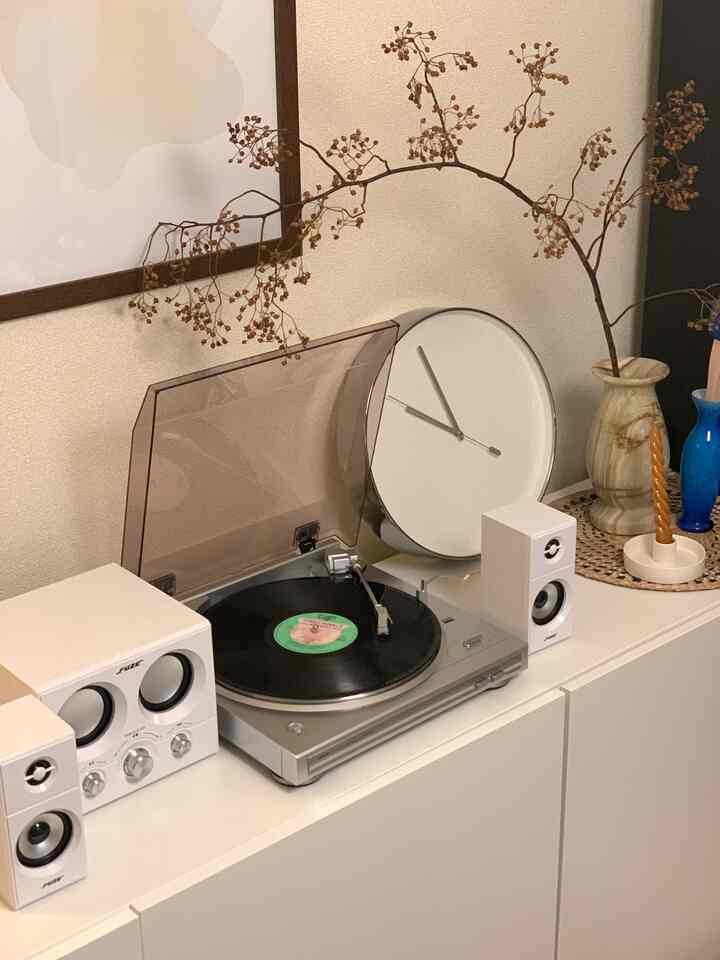 White-toned living room storage featuring a turntable with speakers, wall clock, and candle decor creating a modern retro atmosphere