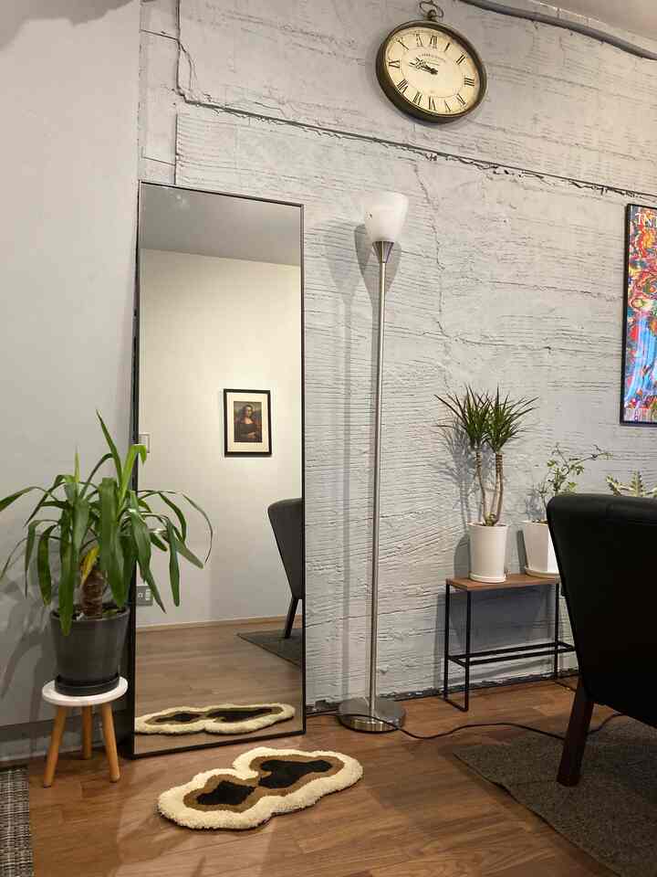 Natural tone living room with wood floor, large standing mirror centrally placed with a small unique rug in front, simple and natural decor
