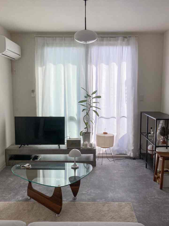 白を基調としたモノトーンのリビング、中央にガラスのコーヒーテーブルとペンダントライトが配置されたシンプルな空間