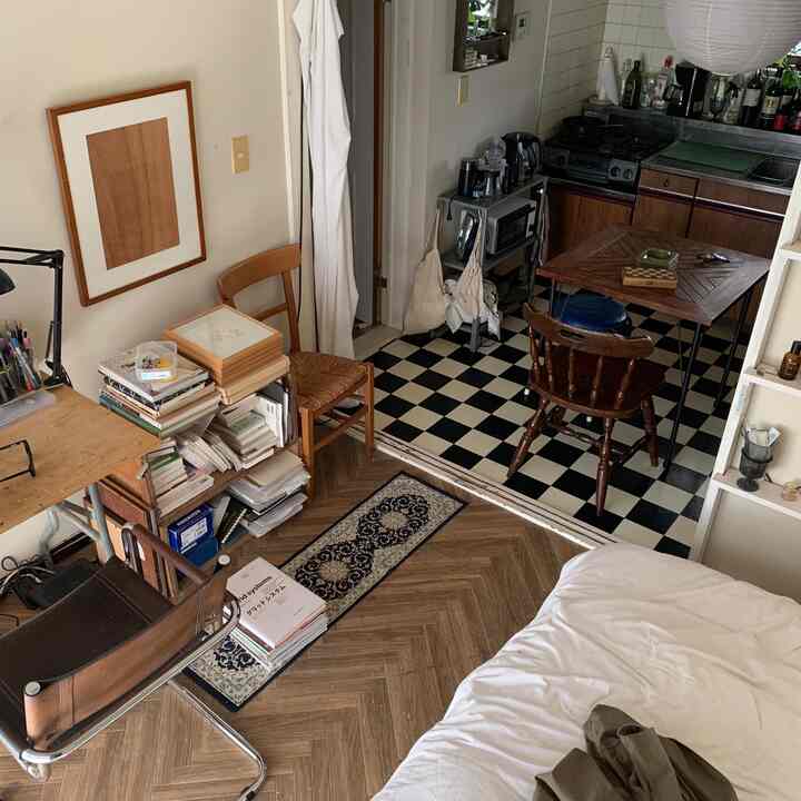 Natural compact studio apartment featuring white bedding, wood-tone furniture, and a small kitchen dining area