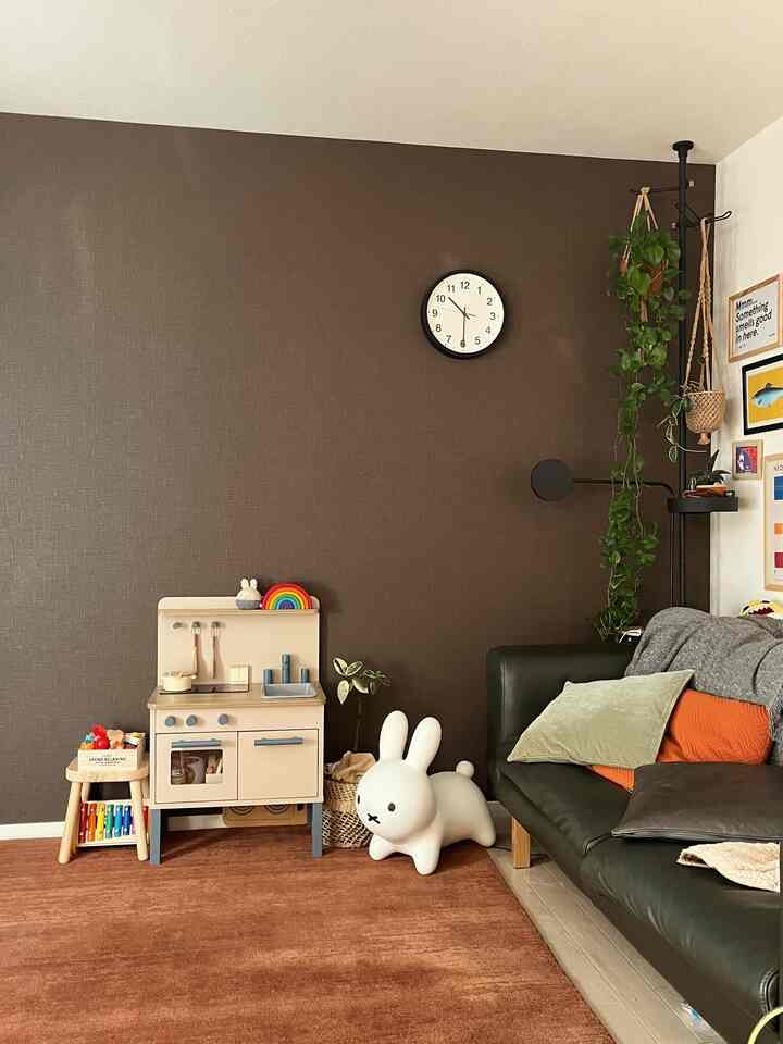 ブラウンのアクセントウォールとラグが特徴的な子供の遊び道具とソファのあるリビングスペース