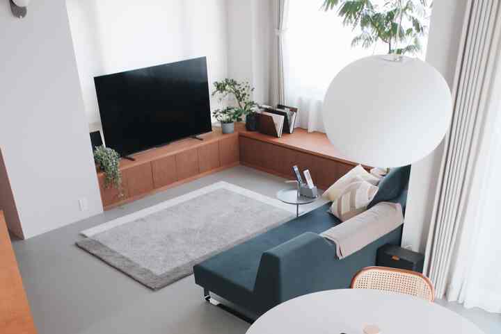 白と木目調の調和が美しいリビング、ダークグリーンのソファとテレビ台が配置されたミニマルで印象的な空間