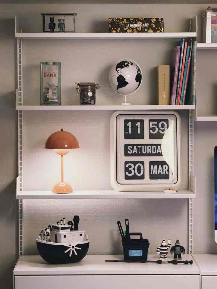 白とオレンジのトーンの棚、時計や様々なオブジェが配置された印象的な空間