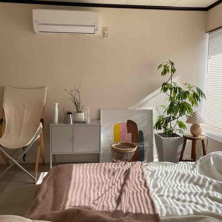 暖かいベージュとホワイトの色調の寝室、ベッドと植物、サイドテーブルが配置された自然な雰囲気のある空間