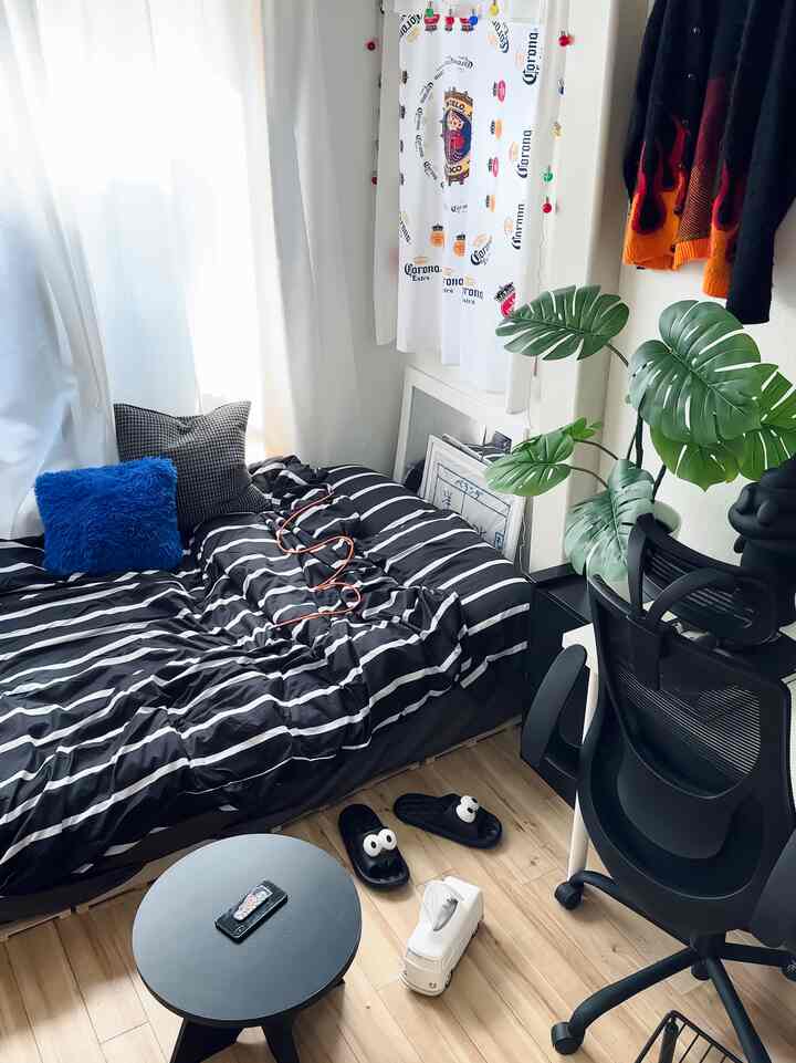 白と黒のトーンで統一された6畳ワンルームの寝室、ストライプの寝具とオフィスチェア、モンステラの植物が配置された落ち着いた空間
