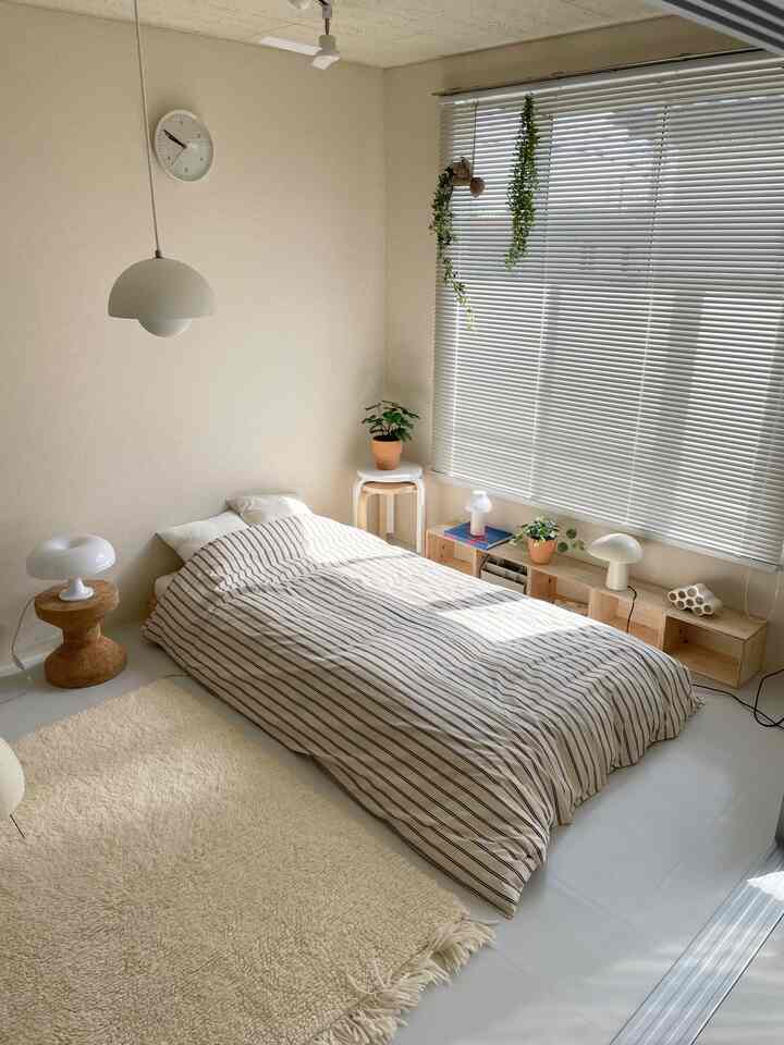 Natural-toned bedroom featuring a striped duvet-covered bed, wood-toned stool, and potted plants creating a cozy atmosphere
