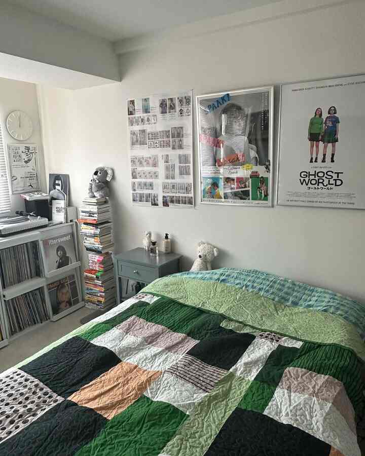 カラフルなベッドカバーがある6畳サイズの一人暮らし寝室、壁に複数のポスターと本棚が配置された雰囲気のあるインテリア
