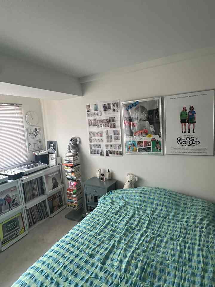 ホワイトの壁にブルーの寝具が配置された6畳の寝室、書棚と壁のデコレーションが調和する雰囲気のあるインテリア